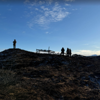 4 personer står på en haug og ser på nedbrente forskningsstrukturer. Det er spor av snø på bakken og blå himmel.